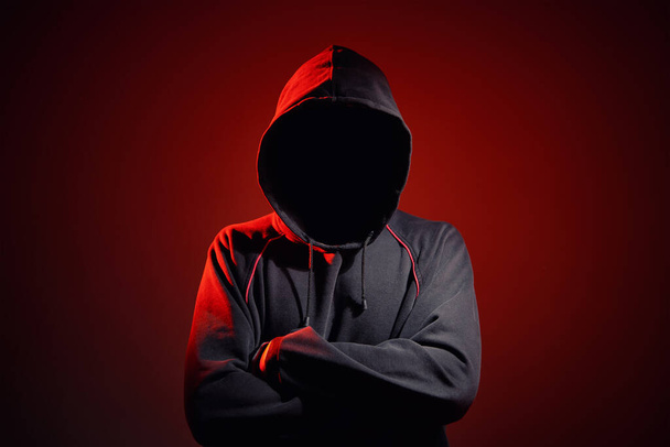 Silhouet af man zonder gezicht in kap op een rode achtergrond. Anonieme misdaadconcept - Foto, afbeelding