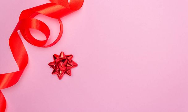 Gift red bow on a pink background and red satin ribbon on the side. Free space for text. Holidays, Christmas, Valentine's Day. - 写真・画像