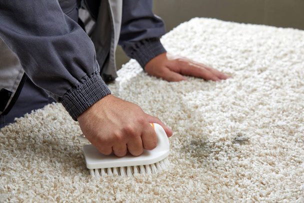 Férfi permetező mosószer a szürke szőnyegen, hogy távolítsa el a foltot a professzionális takarítás szolgáltatás  - Fotó, kép