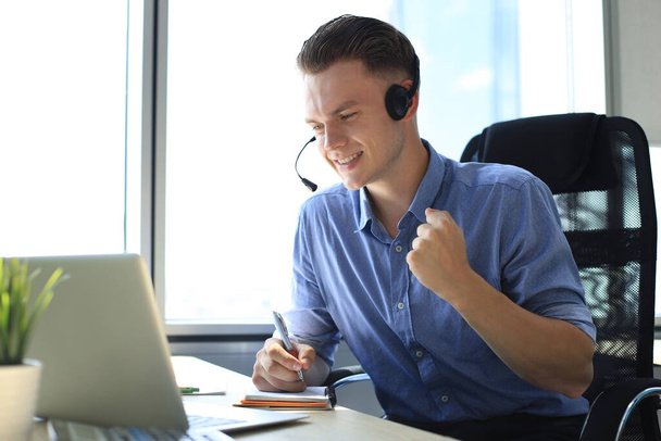 Cheerful young support phone male operator in headset, at workplace while using laptop, help service and client consulting call center concept. - Foto, immagini