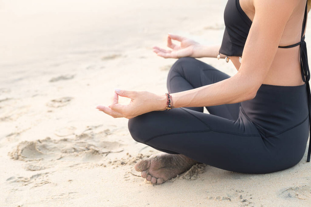 Schlanke reife Frau in Schwarz praktiziert Yoga am Sandstrand Meditation in Nahaufnahme mit Kopierraum - Foto, Bild