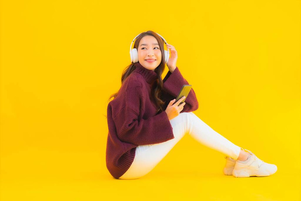 Retrato bonito jovem asiático mulher uso inteligente telefone celular ouvir música no amarelo isolado fundo - Foto, Imagem