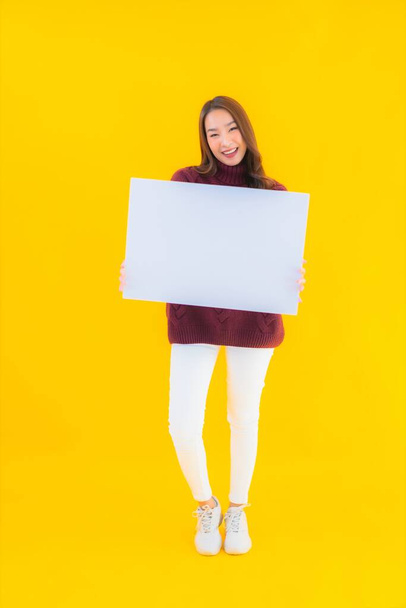 Портрет красива молода азіатка показує порожню білу дошку з паперу на жовтому ізольованому фоні
 - Фото, зображення