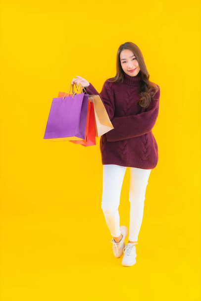 Ritratto bella giovane donna asiatica con colorata shopping bag su sfondo giallo isolato - Foto, immagini