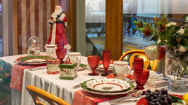Yemek masasının Noel süslemesi. Güzel yeşil servis, cam bardak çatal bıçak takımı. Kırmızı ceketli Noel Baba ve hediyeli bir kutu. - Fotoğraf, Görsel