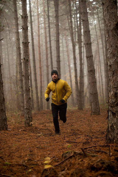 Handsome young man running in autumn forest and exercising for trail run marathon endurance race - Foto, afbeelding