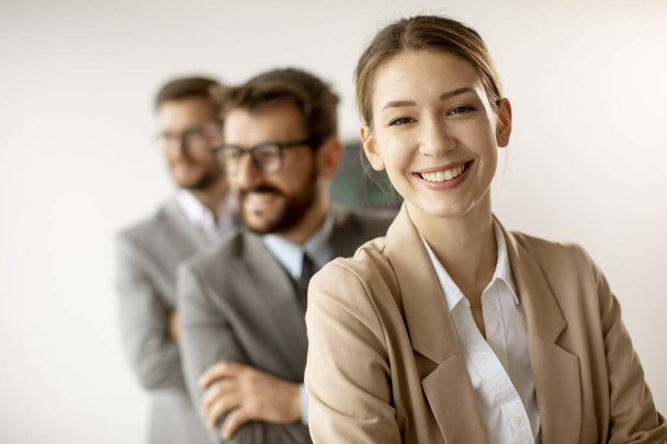 Усміхнена молода бізнес-леді, що стоїть з групою корпоративних колег поспіль разом в офісі
 - Фото, зображення