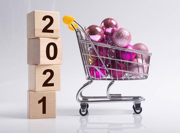 2021 new year with shopping cart or trolley full of miniature christmas baubles or ornaments or balls over white background, side view. - Foto, Bild