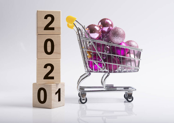 2020 changing for 2021 new year with shopping cart or trolley full of miniature christmas baubles or ornaments or balls over white background, side view. - Фото, зображення