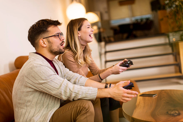 Bella giovane coppia che gioca ai videogiochi a casa, siede sul divano e si diverte - Foto, immagini