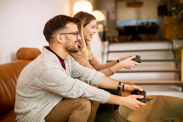 Schönes junges Paar spielt zu Hause Videospiele, sitzt auf dem Sofa und amüsiert sich - Foto, Bild