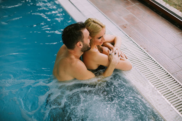 Lovely young couple relaxing on the poolside of interior swimming pool - Foto, immagini