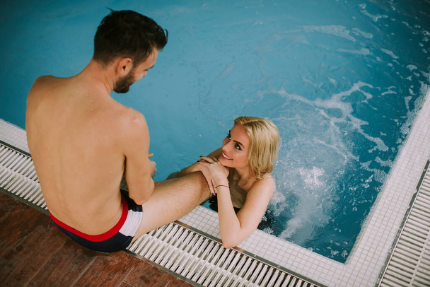 Lovely young couple relaxing on the poolside of interior swimming pool - Photo, Image