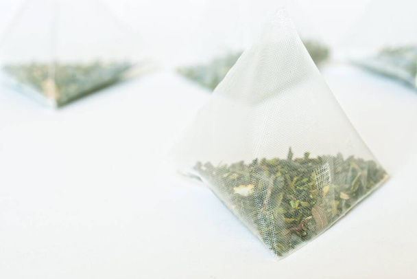 Dreieckige Pyramiden-Teebeutel auf weißem Hintergrund. Grüner Tee mit Kräuter-Aromen. Makro. Geringe Tiefenschärfe  - Foto, Bild
