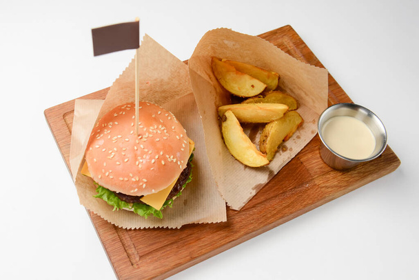 Hamburger with fries and sauce. Juicy burger on a wooden board over white background. Fast food, junk food concept. American style. - Фото, зображення