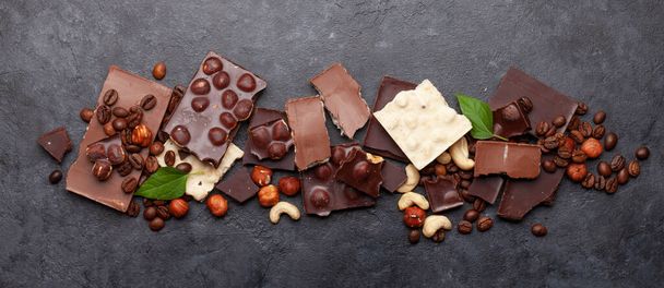 Varios trozos de chocolate, granos de café y nueces en la mesa de piedra. Vista superior plano laico - Foto, Imagen