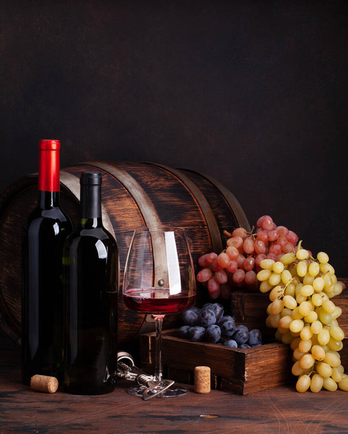 Borosüvegek, szőlő, pohár vörösbor és régi fahordó. Fénymásolási hellyel - Fotó, kép