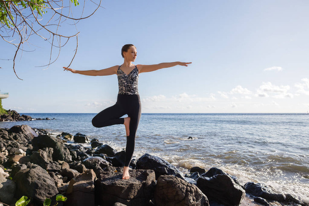 Młoda kobieta w czerni robi jogę na plaży Tree pose ocean view - Zdjęcie, obraz