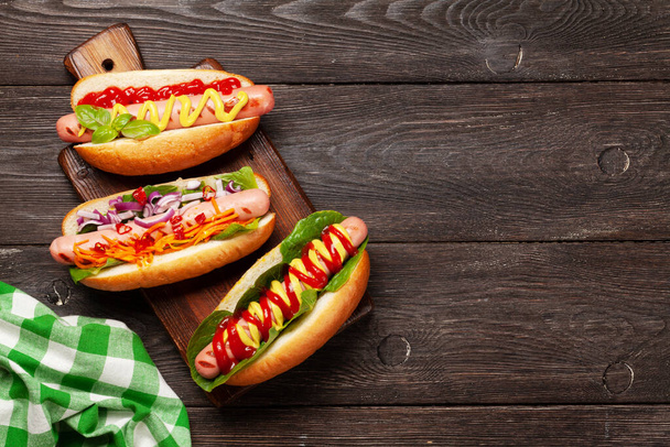 Různé hot dog se zeleninou, salátem a koření na dřevěném pozadí. Horní pohled s místem pro kopírování. Plocha - Fotografie, Obrázek