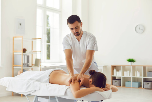 Professional masseur doing therapeutic body massage for young woman lying on massage table - Φωτογραφία, εικόνα