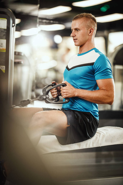 Prise de vue d'un gars musclé en tenue de sport s'entraînant à l'entraînement dur dans la salle de gym. Il pompe les muscles du dos avec un poids lourd. - Photo, image