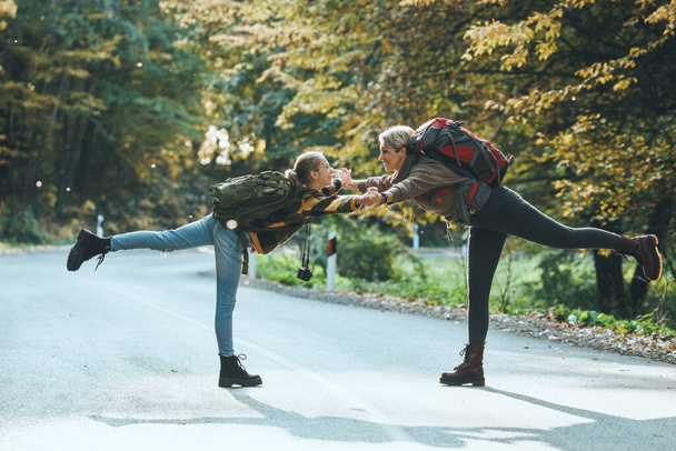 Foto de una alegre adolescente y su madre divirtiéndose y jugando durante el paseo juntos por el bosque en otoño. - Foto, imagen