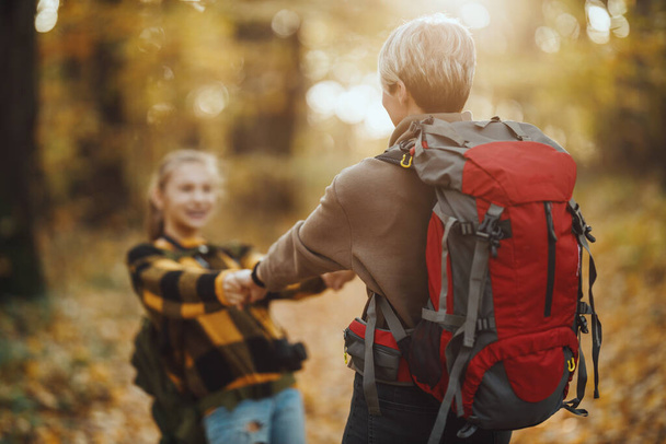 Girato di una ragazza adolescente e sua madre avere fondo durante camminare insieme attraverso la foresta in autunno. - Foto, immagini