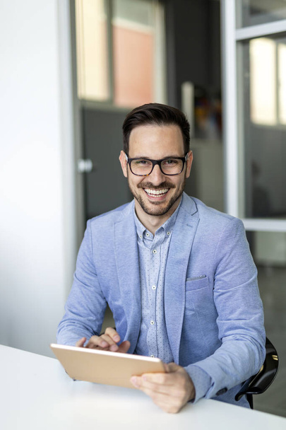 Sourire jeune homme d'affaires en utilisant une tablette numérique dans le bureau - Photo, image