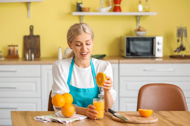 Beautiful young woman making fresh orange juice in kitchen - Fotó, kép