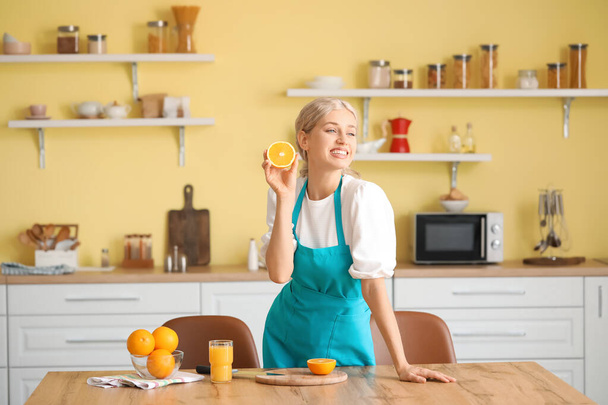 Beautiful young woman with oranges and juice in kitchen - Foto, afbeelding