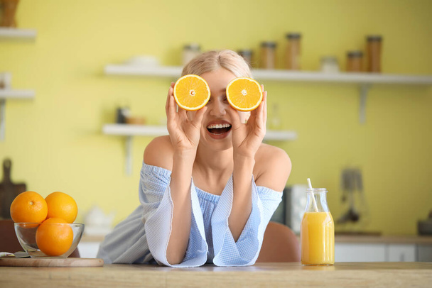 Funny young woman with oranges and juice in kitchen - Foto, afbeelding