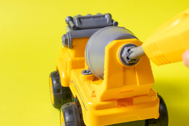De speelgoedschrijfmachine is een betonmixer en schroevendraaier die het radertje op een gele achtergrond verdraait. Foto 's voor een speelgoedwinkel en educatieve activiteiten. Vroege ontwikkeling van kinderen - Foto, afbeelding