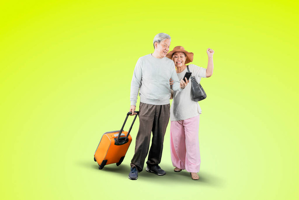 Old couple using a smartphone with happy expression while carrying a luggage in the studio with green screen background - Foto, Imagem