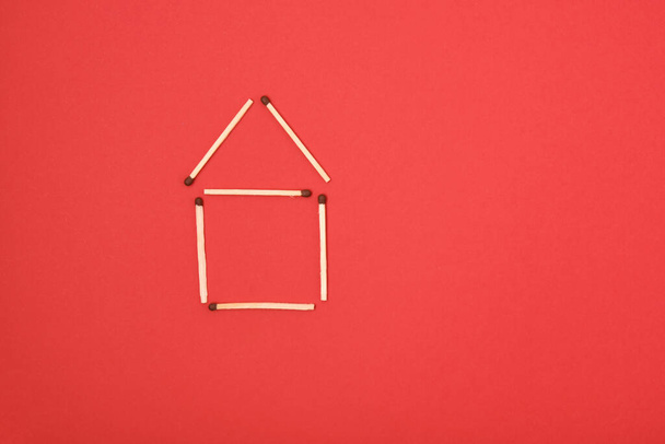 silhouette of a house made of matches on a red background copy space - Photo, image