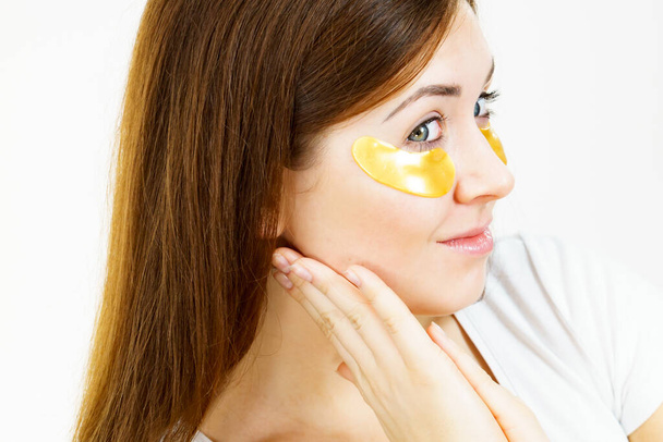 Young woman with golden collagen patches, under eye pads. Mask removing wrinkles and dark circles. Girl taking care of delicate skin around eyes. Beauty treatment. - Foto, Imagem