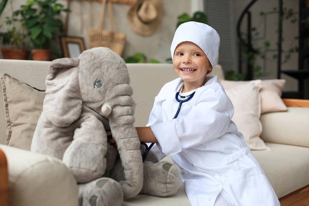 Adorable niño vestido de médico jugando con elefante de juguete, comprobando su respiración con estetoscopio - Foto, imagen