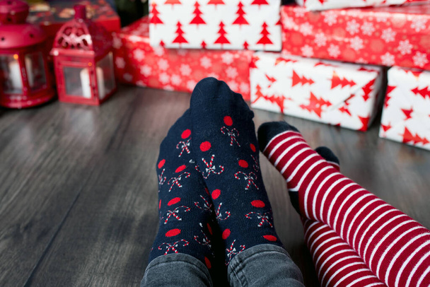 Feet wearing Christmas socks on plaid. Mother and child sitting together and prepare gifts. People relaxing at home - 写真・画像