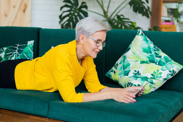 beautiful adult woman with short hair is lying on the couch with a tablet - Φωτογραφία, εικόνα