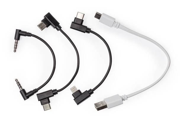 Набір різних коротких адаптерних кабелів - різні USB, USB Type-C до Lightning, аналоговий аудіокабель з міні-роз'ємами на білому тлі, вид зверху
 - Фото, зображення