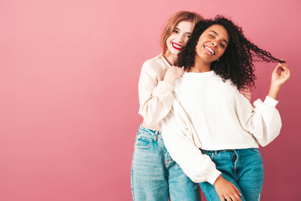 Two young beautiful smiling international hipster female in trendy summer jeans clothes. Sexy carefree women posing near pink wall in studio. Positive models having fun. Concept of friendship  - 写真・画像