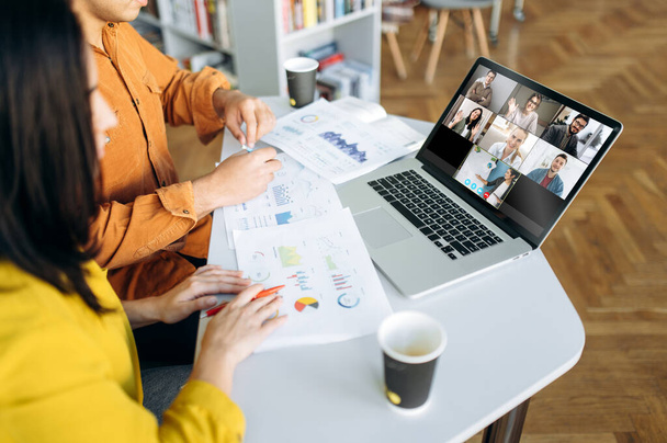 Online video chat. Laptop monitor view with multiracial business colleagues discussing about financial graphs, man and woman sitting on their workplace during video conference - Foto, Imagem