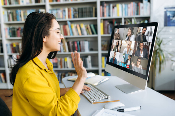 Ηλεκτρονική εκπαίδευση. Μια φοιτήτρια που μαθαίνει online στο σπίτι, χαιρετάει άλλους μαθητές ή συναδέλφους στην οθόνη του υπολογιστή σε τηλεδιάσκεψη και χαμογελά - Φωτογραφία, εικόνα