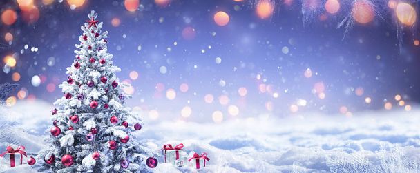 Verschneiter Weihnachtsbaum mit rotem Ornament und Geschenkschachteln in einer Winterlandschaft - Foto, Bild
