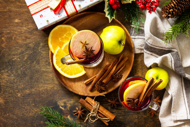 Winterse kerstdrank met sinaasappel, appel en specerijen. Glühwein in glazen mok met specerijen op rustieke tafel. Bovenaanzicht vlak. Kopieerruimte. - Foto, afbeelding