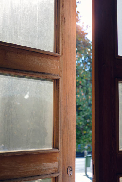 Открытая деревянная дверь с пыльным стеклом на фоне размытой улицы - Фото, изображение