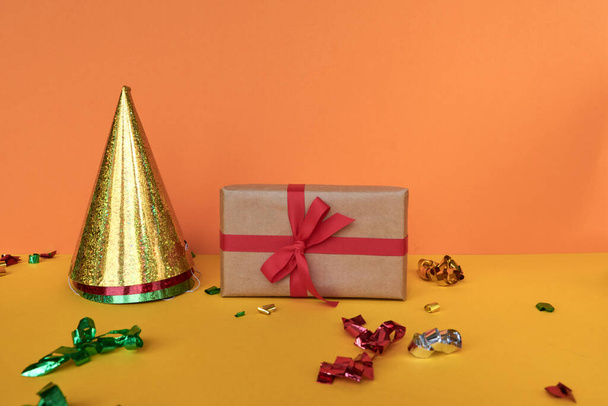Рождественская композиция Подарок с красной лентой и конфетти украшения на пастельной бумаге красочный фон. Рождество, зима, новогодние праздники. Плоская кладка, вид сверху, копировальное пространство. - Фото, изображение