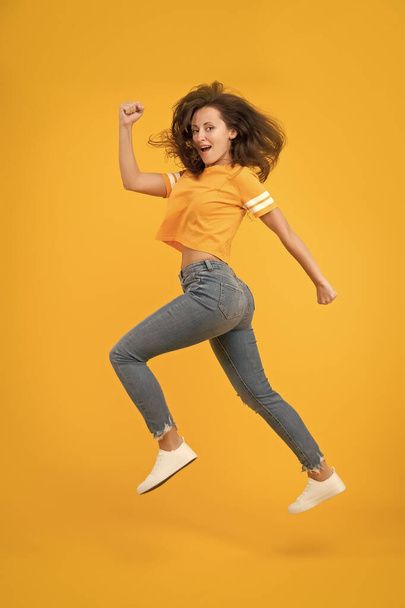 Feel inner energy. Energetic woman running or jumping. Skinny jeans suits her. Sexy girl yellow background. Sensual girl in casual style. Pretty girl with long hair. Fashion style. Beauty and make up - Zdjęcie, obraz