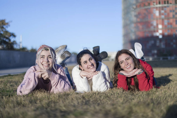 Group of three beautiful young women lie on the lawn, resting and daydreaming in the park on the green grass. - Foto, Bild