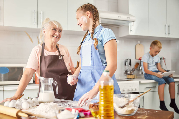 Happy girl and her smiley grandmother posing in kitchen - Zdjęcie, obraz