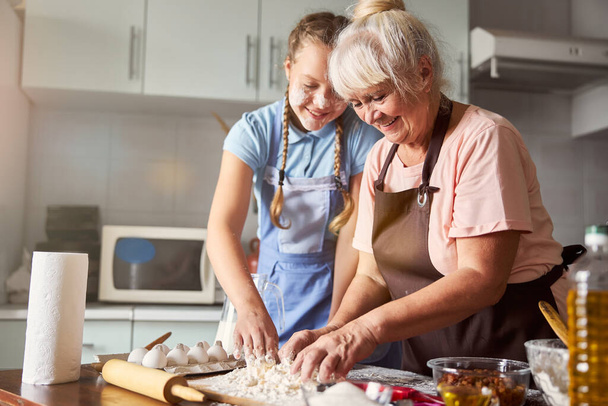Zufriedene Großmutter lässt ihre Enkelin in der Küche helfen - Foto, Bild